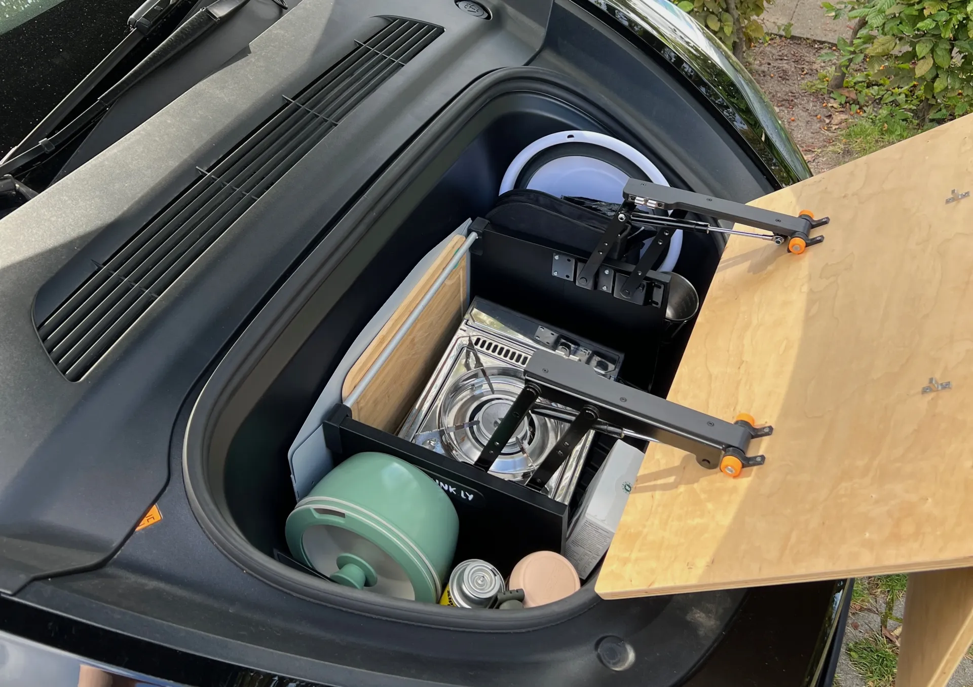 Tesla Model 3 frunk with Frunkly table set up as outdoor kitchen with camp stove, pot, and cutting board