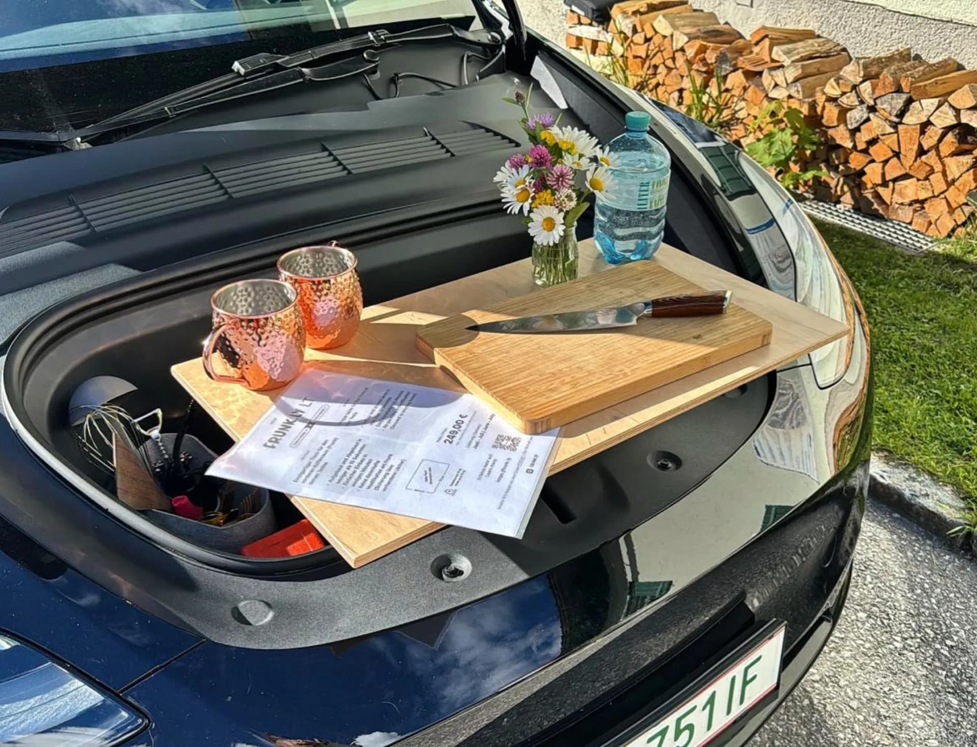 Frunkly table on Tesla frunk with copper mugs, cutting board, and wildflowers